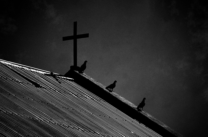 Tin roofed church in Taree, South Australia with three doves arranged in a straight line facing away from a cross