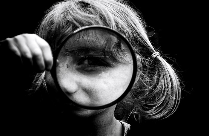 A girl hold a magnifying glass up to one eye. The window into the soul, magnified.