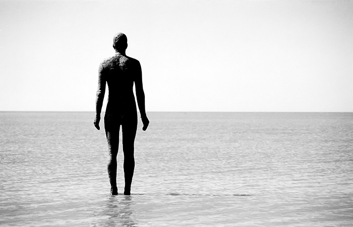 A single statue looks out on an empty sea. From sculpture Antony Gormley's 100-strong installation, 'Another Place' at Crosby Beach in England.