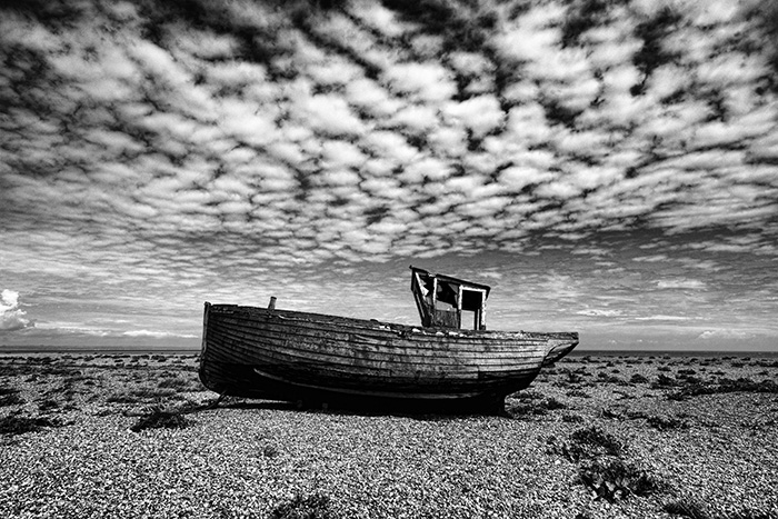 Decaying fishing boat under a mackerel sky on the shingle beach at Dungeness in England