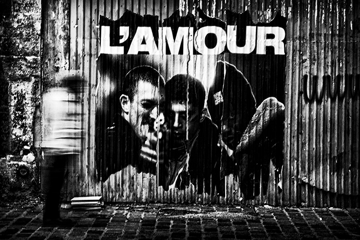 Motion-blurred man walking past a poster for the film La Haine with the word L'Amour above