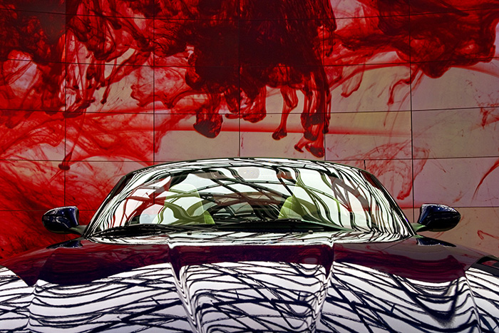 Low front view of a sports car against a giant plasma screen showing a moving pattern of red blood