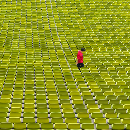 A lone man in red walks among a sea of green seating