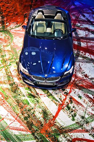 A BMW Roadster viewed from above front, parked on top of the artwork created by painting the wheels and driving on a canvas