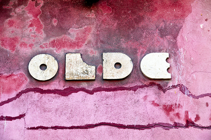 A decaying pink wall embossed in white with the word 'OLDE'