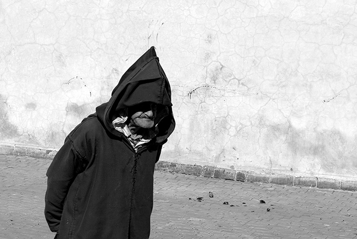 Old man in traditional clothing walks by in a candid street scene from the medina in the coastal town of Essaouira, Morocco