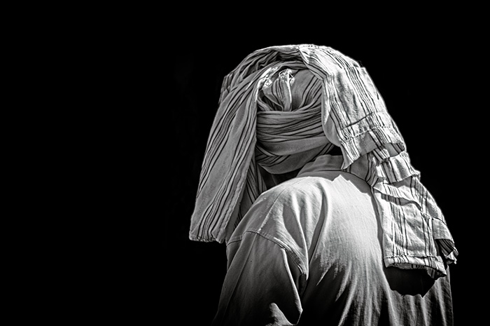 Head and shoulder shot of a man with Arabic style headwear viewed from behind against a black background