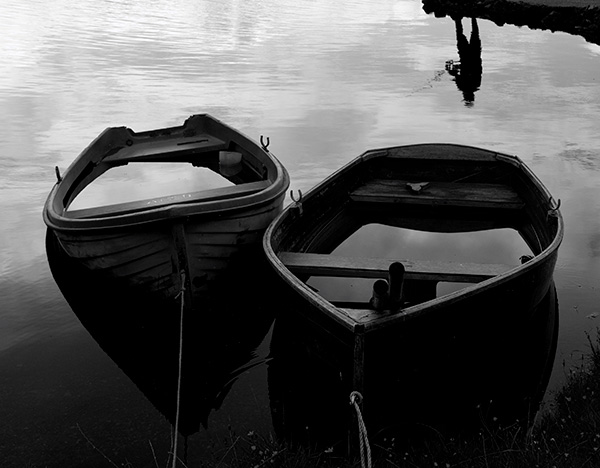 Inverted reflection of fisherman and two boats filled with water at a loch in the North West Highlands of Scotland