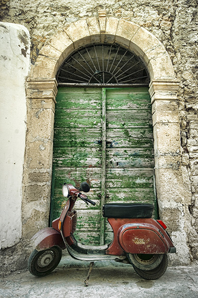 A dilapidated motor scooter parked in front of a badly weathered door
