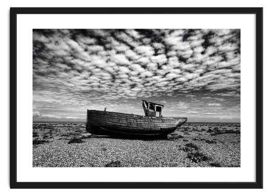 Framed image of a decaying fishing boat under a mackerel sky on the shingle beach at Dungeness in England