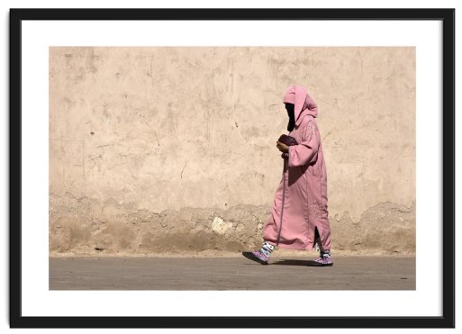 A woman in traditional Moroccan pink clothing wals along with a bare stone wall background