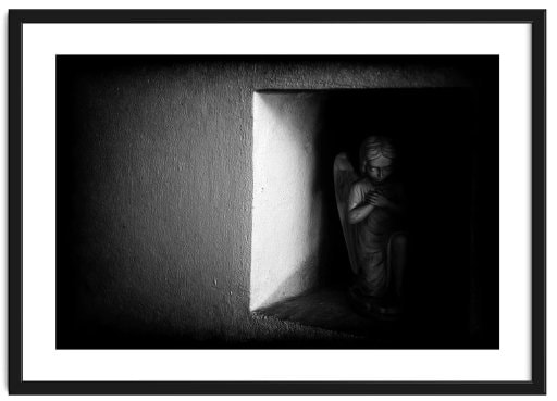 Framed image of a semi-lit statuette of a kneeling angel in the wall alcove of an ancient church