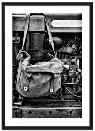 An old canvas bag hangs next to the exposed engine of a vintage tractor