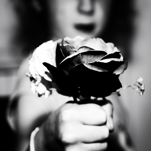 A blurred woman hold out a hand containing a flower