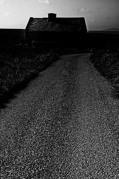 Dark scene of a road leading to the silhouette of a derelict house