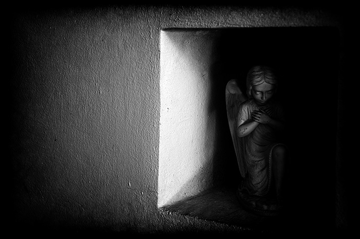 Semi-lit statuette of a kneeling angel in the wall alcove of an ancient church