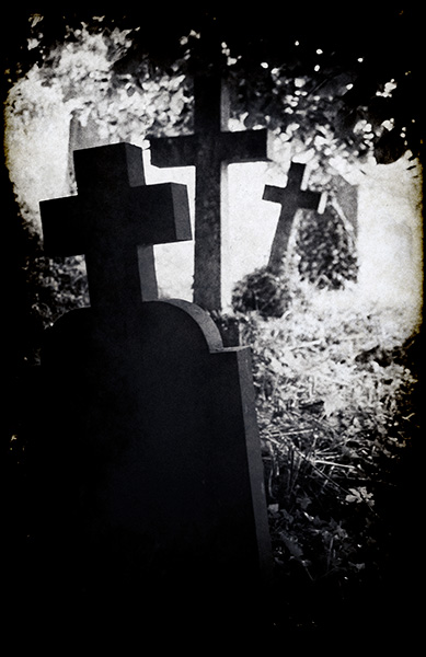 Dark moody image of an old, unkempt graveyard with three lopsided crosses