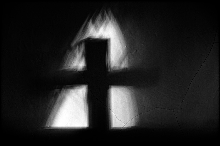 The shadow of a cross on the bare wall of an ancient church gives the illusion of being on fire
