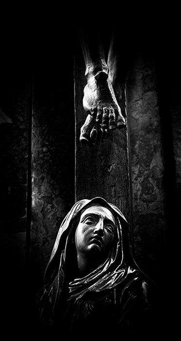 A statue of Virgin Mary looking upward at the feet of Jesus on the cross