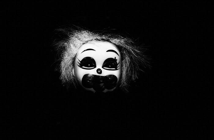 Portrait of a toy clown with exaggerated features, surrounded by blackness