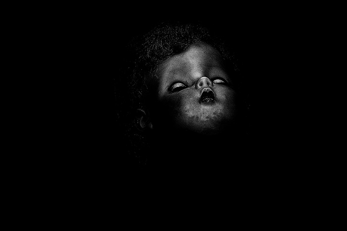 Grainy portrait of a sleeping doll photographed from a low angle , surrounded by blackness