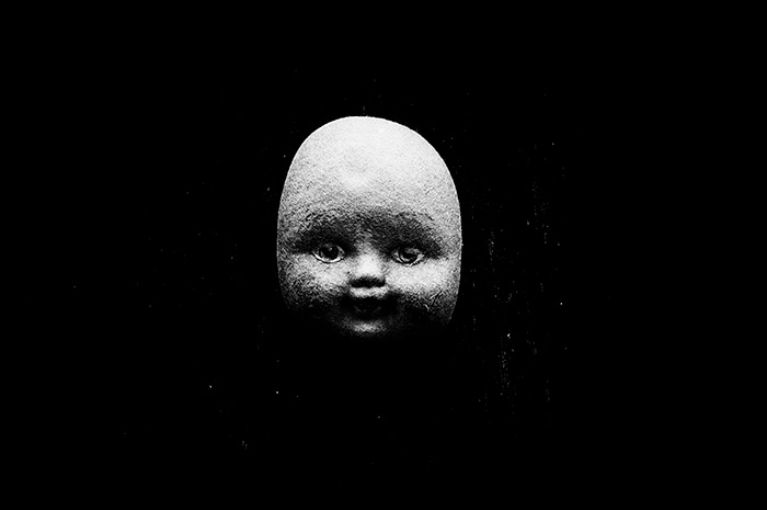 Portrait view of a bald doll with eyes staring ahead, surrounded by blackness