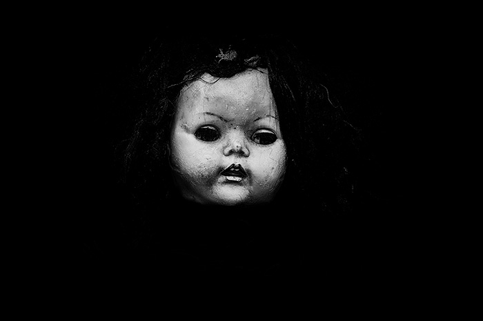 Portrait of a grotesque looking vintage doll surrounded by blackness