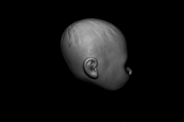Profile of a bald plastic doll surrounded by blackness