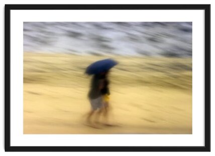 Blurred, impressionist style image of two people waling along a beach covered with an umbrella