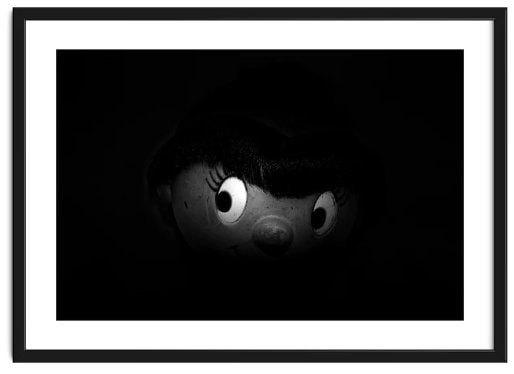 Framed image of a partly lit Noddy face with eyes looking sideways surrounded by blackness