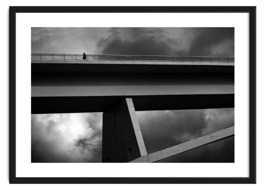 A giant concrete bridge with a single silhouetted lone figure walking along the top, against a menacing dark sky