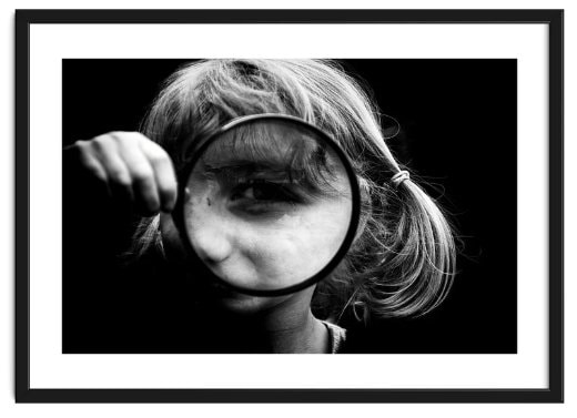 Framed image of a girl hold a magnifying glass up to one eye. The window into the soul, magnified.