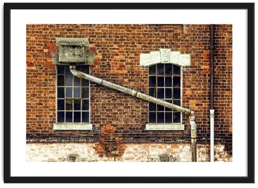 A derelict, weathered brick factory building with prominent guttering