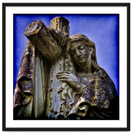 Stone statue covered in lichen of a woman hugging a cross against a blue background